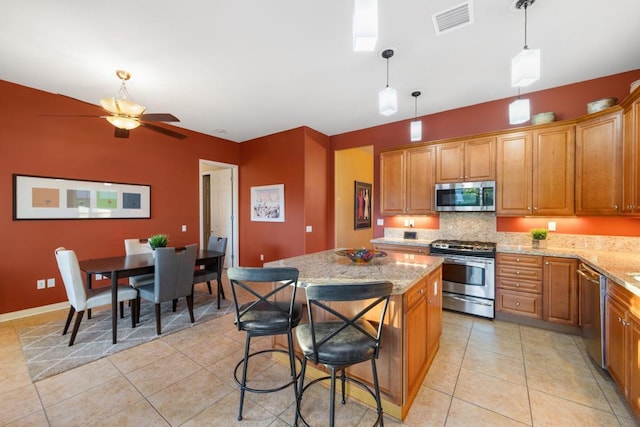 kitchen featuring light stone countertops, appliances with stainless steel finishes, a center island, and pendant lighting