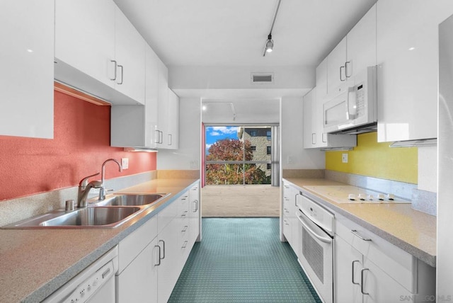 kitchen with sink, white appliances, rail lighting, white cabinets, and dark tile patterned flooring