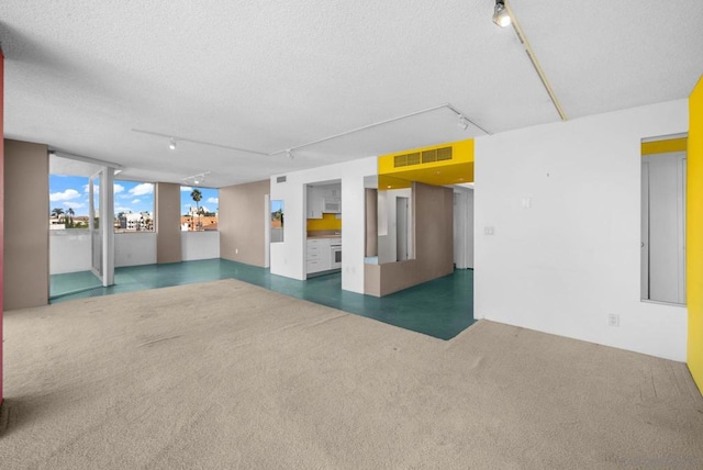 empty room with rail lighting, a textured ceiling, and dark colored carpet