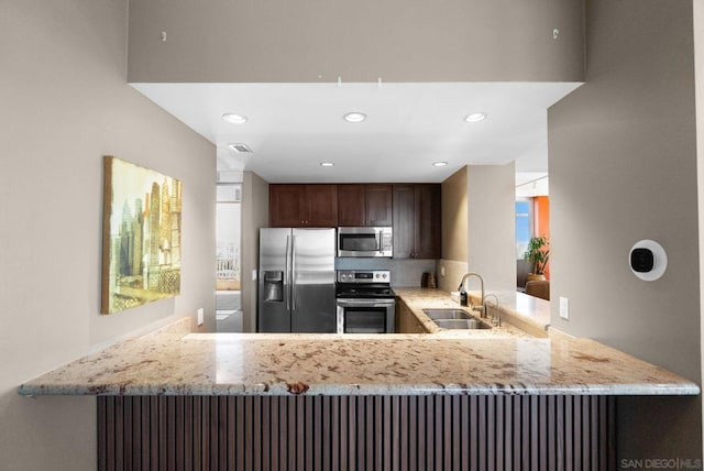 kitchen featuring stainless steel appliances, sink, light stone counters, and kitchen peninsula