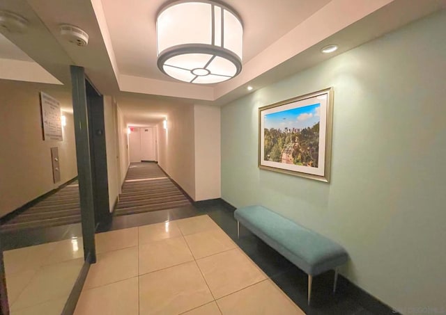 hallway with tile patterned flooring and a tray ceiling