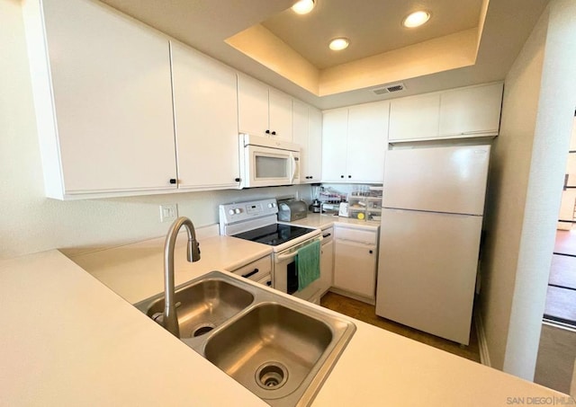 kitchen with a raised ceiling, white cabinetry, sink, and white appliances