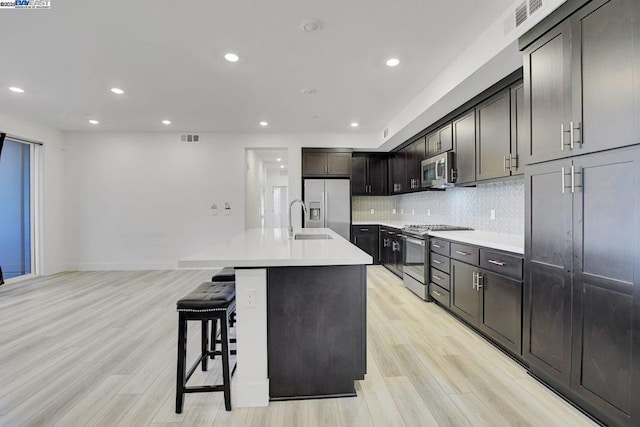 kitchen featuring sink, stainless steel appliances, a kitchen breakfast bar, an island with sink, and light wood-type flooring