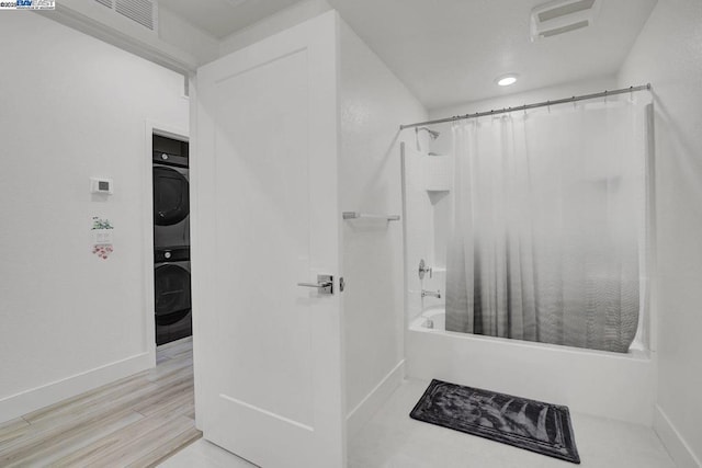 bathroom featuring wood-type flooring, shower / bathtub combination with curtain, and stacked washer / dryer