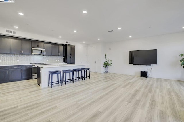 kitchen featuring a center island with sink, a breakfast bar area, appliances with stainless steel finishes, and light hardwood / wood-style flooring