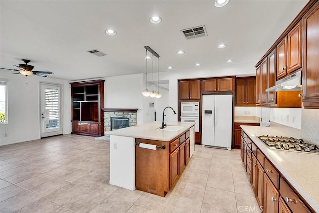 kitchen featuring under cabinet range hood, white appliances, a sink, light countertops, and decorative light fixtures