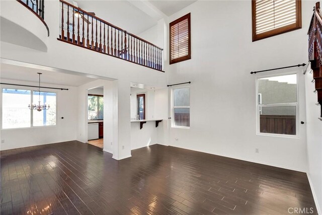 unfurnished living room featuring a high ceiling, dark hardwood / wood-style flooring, and an inviting chandelier