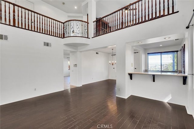 unfurnished living room with a high ceiling, dark wood-style flooring, visible vents, and a notable chandelier