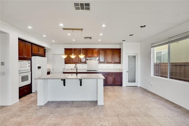 kitchen featuring white appliances, decorative light fixtures, a kitchen bar, an island with sink, and sink