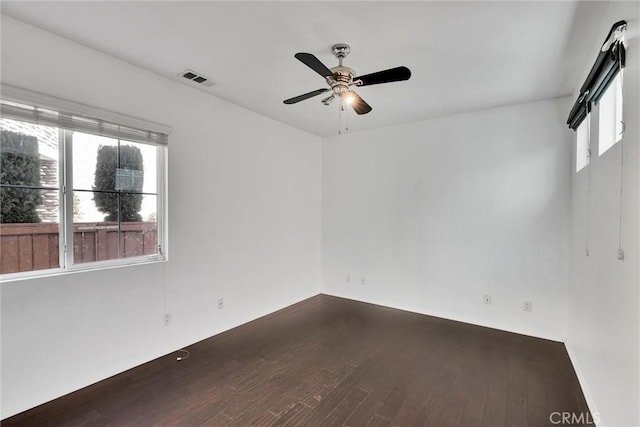 spare room featuring a healthy amount of sunlight, ceiling fan, visible vents, and dark wood-type flooring