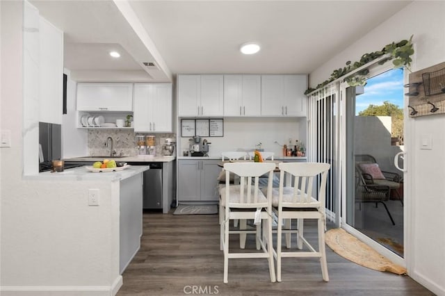 kitchen featuring dark wood-type flooring, stainless steel dishwasher, tasteful backsplash, and white cabinets