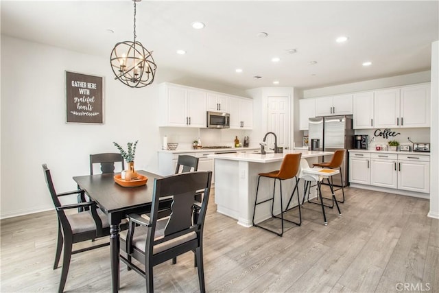 kitchen with appliances with stainless steel finishes, light wood-type flooring, pendant lighting, a center island with sink, and white cabinets