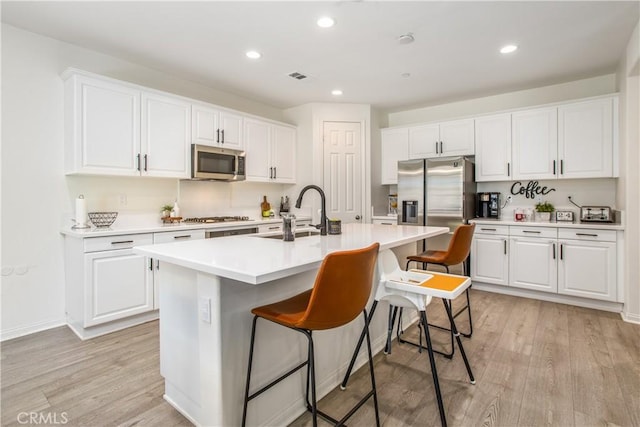 kitchen with white cabinets, stainless steel appliances, a kitchen island with sink, and sink