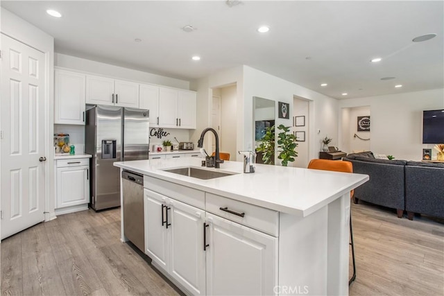 kitchen featuring sink, stainless steel appliances, a kitchen island with sink, white cabinets, and light wood-type flooring