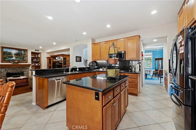 kitchen featuring a center island, stainless steel appliances, a stone fireplace, kitchen peninsula, and dark stone countertops