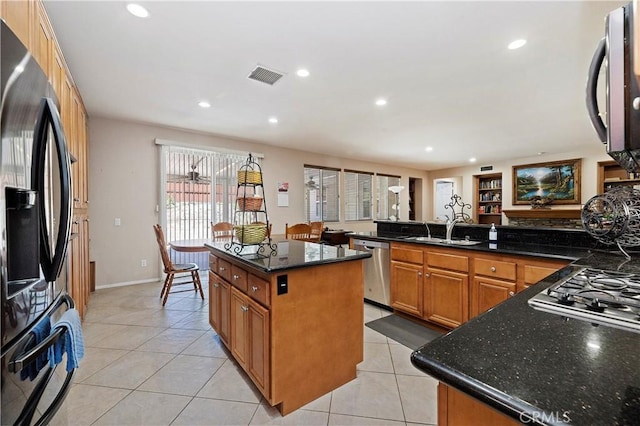 kitchen with sink, stainless steel appliances, a kitchen island, dark stone countertops, and light tile patterned flooring