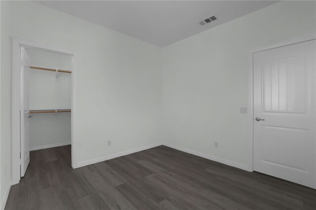 unfurnished bedroom with a walk in closet, a closet, and dark wood-type flooring