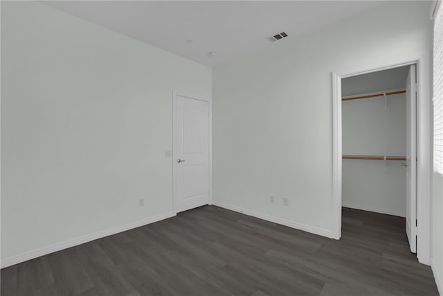 unfurnished bedroom featuring a walk in closet, dark hardwood / wood-style flooring, and a closet