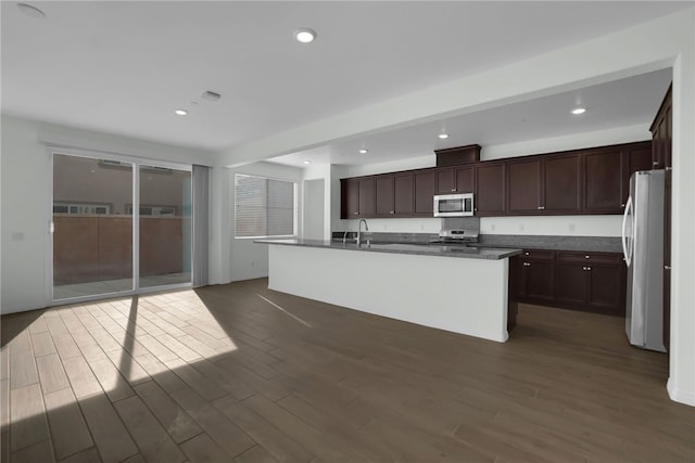 kitchen featuring dark hardwood / wood-style flooring, stainless steel appliances, and a center island with sink