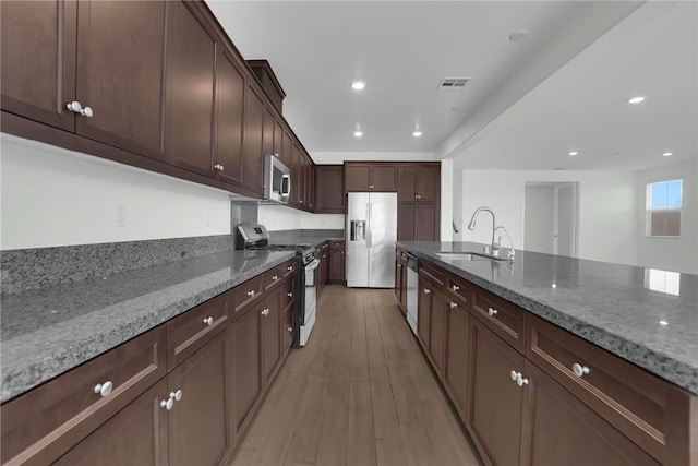 kitchen featuring stone counters, sink, light wood-type flooring, appliances with stainless steel finishes, and dark brown cabinetry