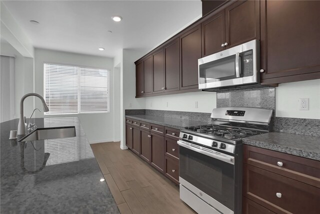 kitchen with appliances with stainless steel finishes, dark brown cabinets, dark stone counters, and sink