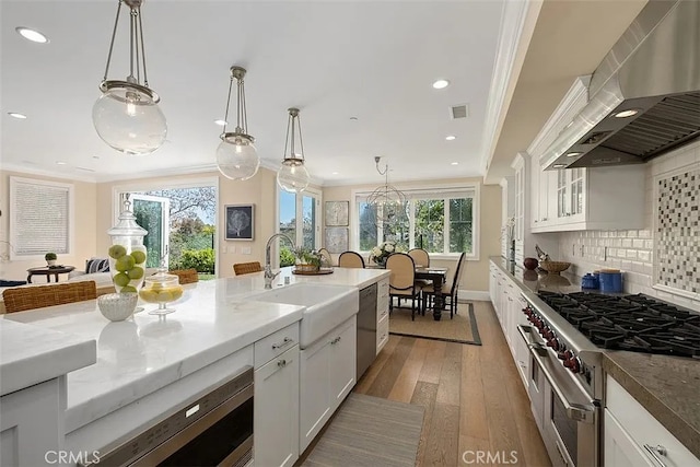 kitchen featuring sink, wall chimney exhaust hood, decorative light fixtures, white cabinetry, and stainless steel appliances