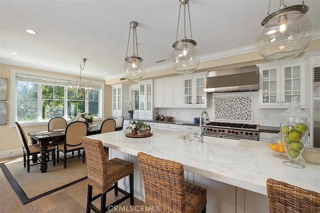 kitchen with stainless steel stove, wall chimney range hood, light stone counters, pendant lighting, and white cabinets