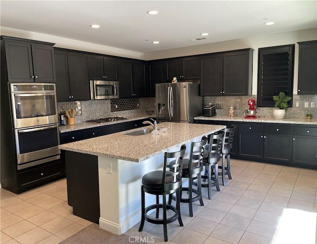 kitchen featuring sink, light tile patterned floors, a kitchen island with sink, stainless steel appliances, and a kitchen bar