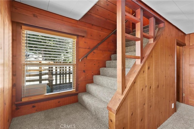 stairway featuring lofted ceiling, carpet flooring, and wood walls