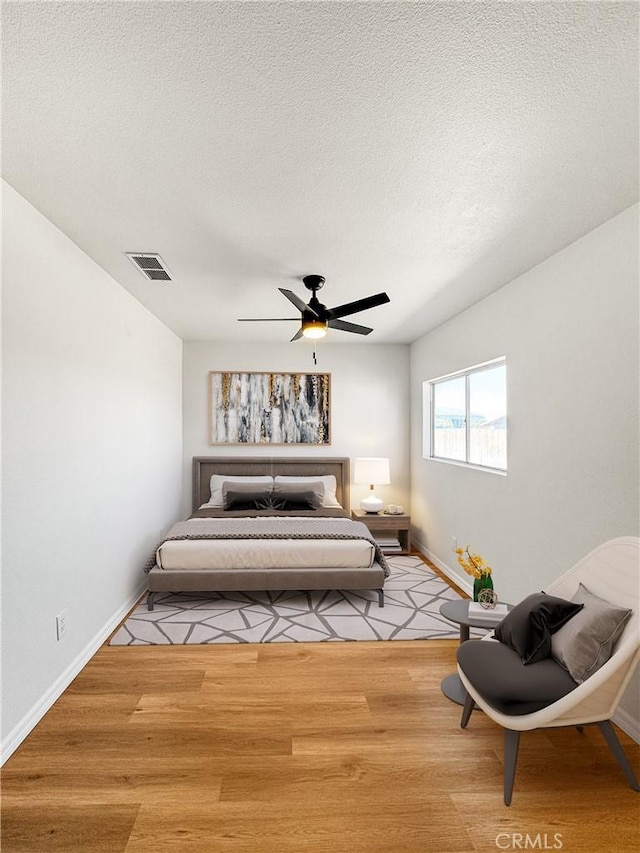 bedroom with a textured ceiling, light wood-type flooring, and ceiling fan