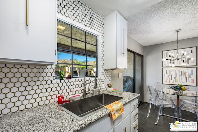 kitchen with backsplash, sink, hanging light fixtures, a textured ceiling, and white cabinetry