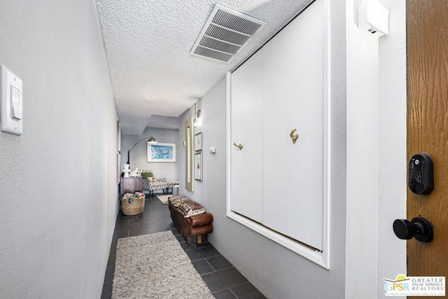 hall featuring a textured ceiling and dark tile patterned flooring