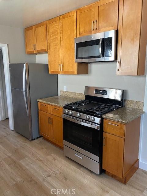 kitchen with light stone counters, stainless steel appliances, and light hardwood / wood-style floors