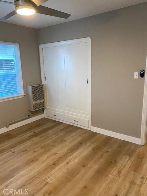 unfurnished bedroom featuring a wall unit AC, ceiling fan, a closet, and light wood-type flooring