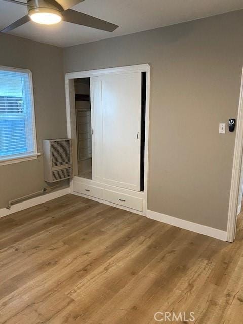 unfurnished bedroom featuring heating unit, ceiling fan, a closet, and hardwood / wood-style flooring