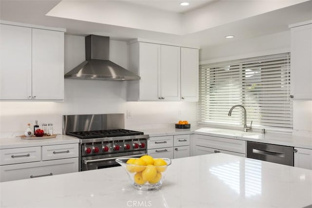 kitchen with a sink, white cabinets, appliances with stainless steel finishes, light stone countertops, and wall chimney exhaust hood