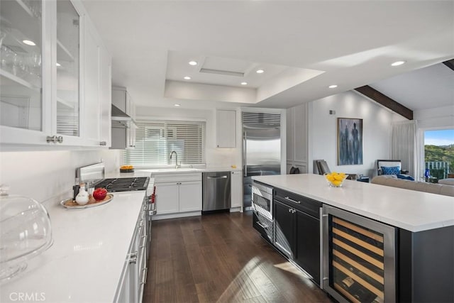 kitchen with wine cooler, a raised ceiling, light countertops, a kitchen island, and built in appliances