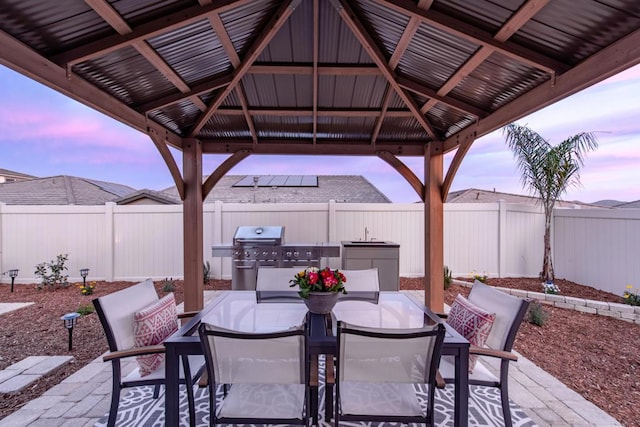 patio terrace at dusk with sink, grilling area, and a gazebo