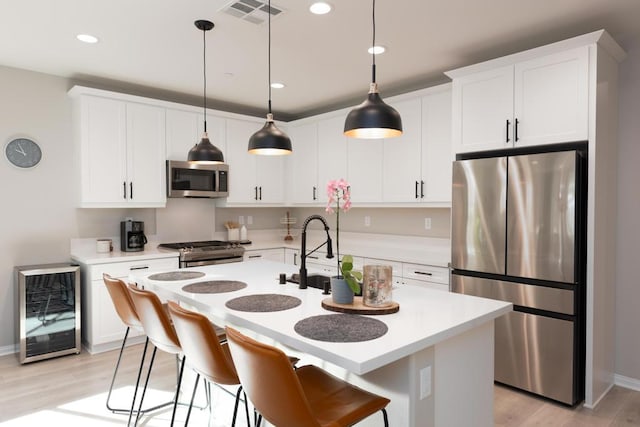 kitchen with white cabinets, light wood-type flooring, hanging light fixtures, wine cooler, and appliances with stainless steel finishes