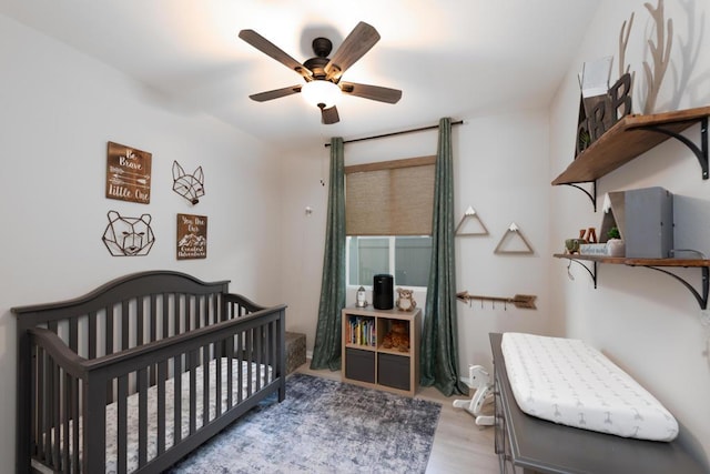 bedroom featuring ceiling fan, light hardwood / wood-style flooring, and a crib