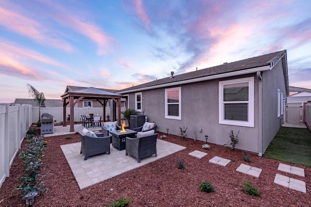 back house at dusk with a gazebo, central air condition unit, an outdoor fire pit, and a patio area