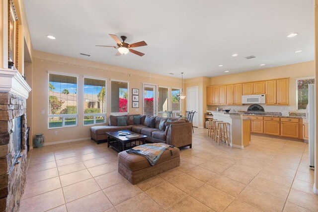 living room featuring ceiling fan, light tile patterned floors, and a stone fireplace