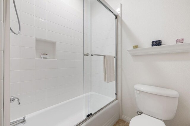 bathroom with toilet and combined bath / shower with glass door