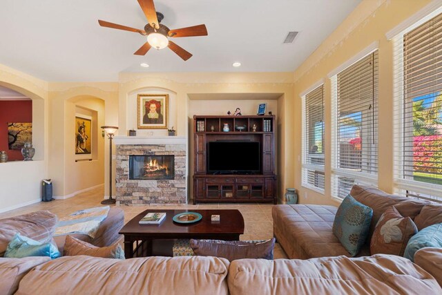 tiled living room featuring ceiling fan and a stone fireplace