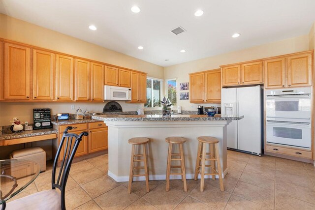 kitchen featuring a breakfast bar area, white appliances, light tile patterned flooring, stone countertops, and a kitchen island