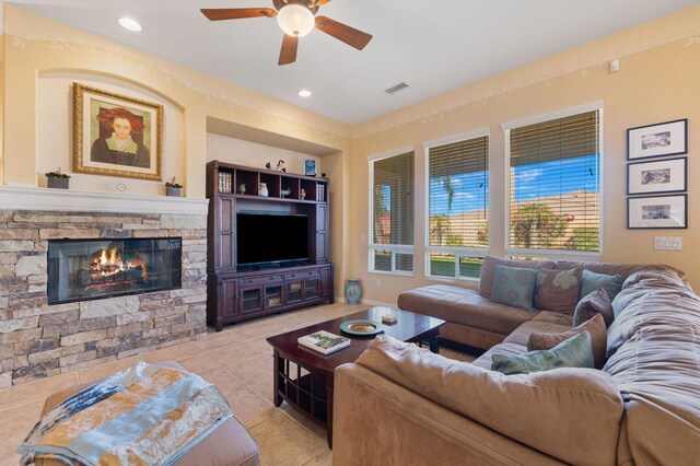 tiled living room featuring ceiling fan, built in features, and a stone fireplace