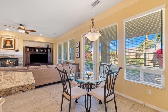 dining space with ceiling fan, light tile patterned flooring, a wealth of natural light, and a fireplace