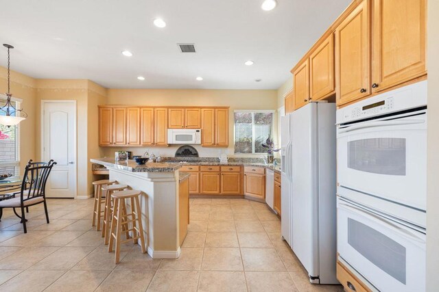 kitchen featuring a kitchen bar, light brown cabinets, decorative light fixtures, white appliances, and a kitchen island