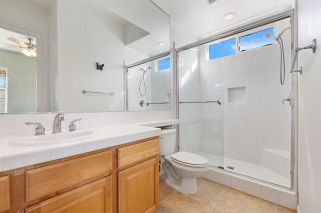 bathroom with a shower with shower door, tile patterned floors, vanity, toilet, and ceiling fan