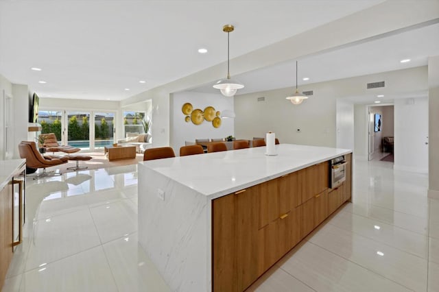 kitchen featuring stainless steel oven, light tile patterned floors, a spacious island, and decorative light fixtures